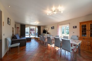A spacious living area with a sofa, dining table, chairs, and a kitchen area.
