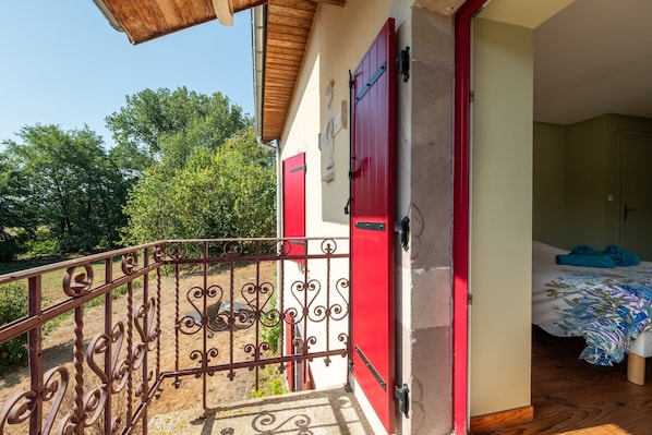 A room with a bed, a red door, and a balcony with a wrought iron railing.