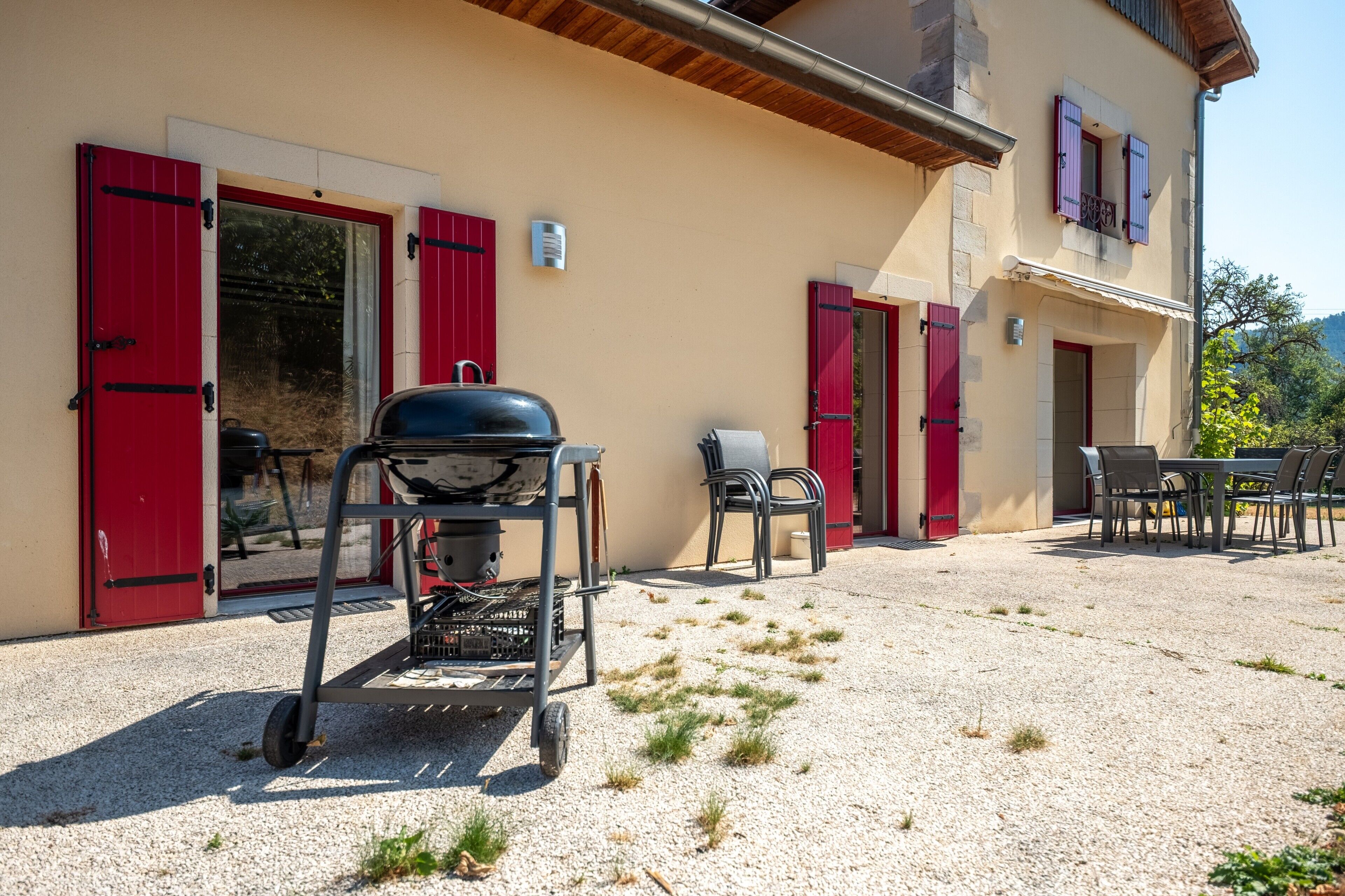 Une terrasse avec un barbecue, des meubles d’extérieur et un bâtiment aux volets rouges.