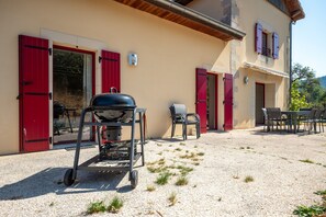 A patio with a barbecue grill, outdoor seating, and a building with red shutters.