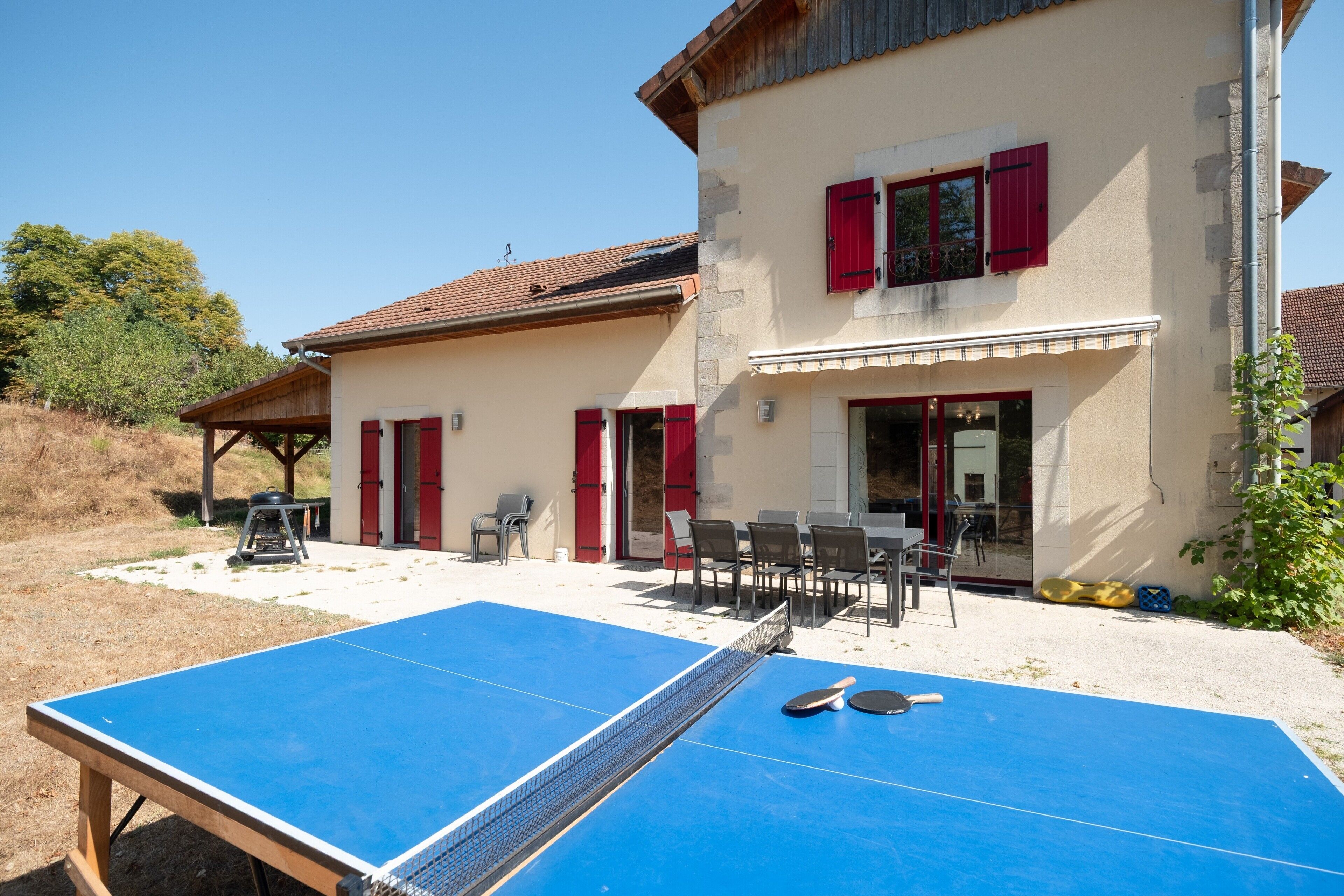 A house with a tennis court, outdoor seating, and a barbecue grill.