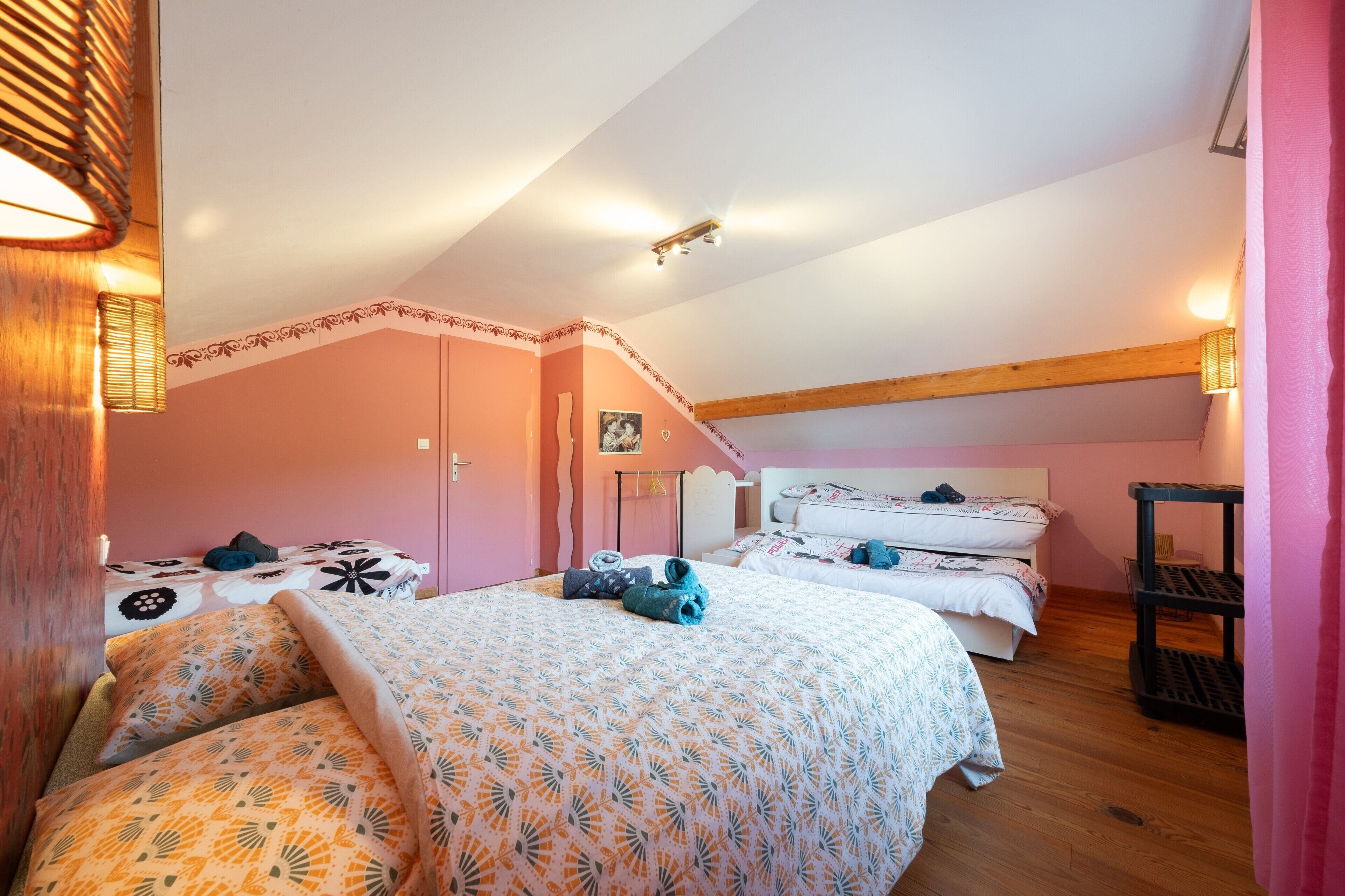 Une chambre avec deux lits, un plafond en bois et un mur rose.