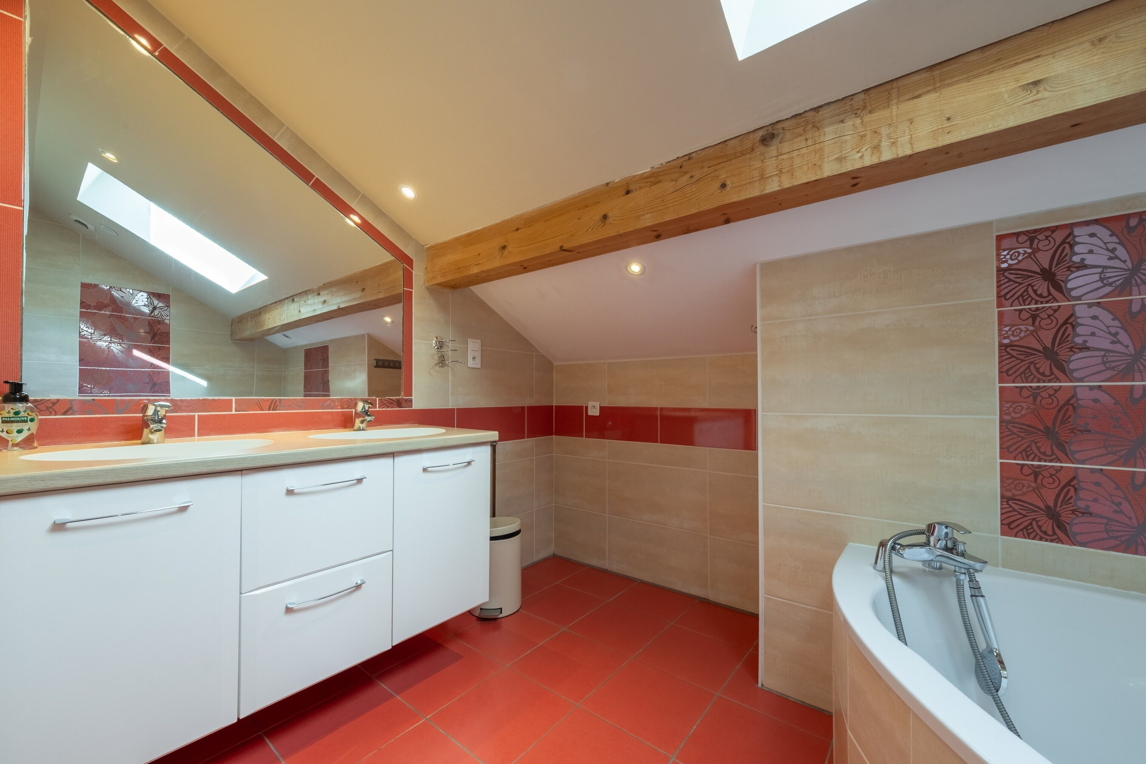 A modern bathroom with a wooden ceiling, a bathtub, a sink with a mirror, and red-tiled walls.
