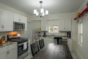 A modern kitchen with white cabinets, a stainless steel range, a built-in microwave, and a dining area with a dark wood table and chairs. - 1 Mi to Notre Dame: 4BR, Private Yard & Pets (South Bend)