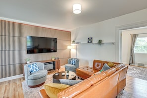 Una sala de estar moderna con una televisión de pantalla plana, dos sillones, un sofá, una mesa de centro y una estantería.