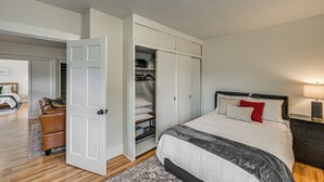 A bedroom with a bed, bedside table, and an open closet with hanging clothes.