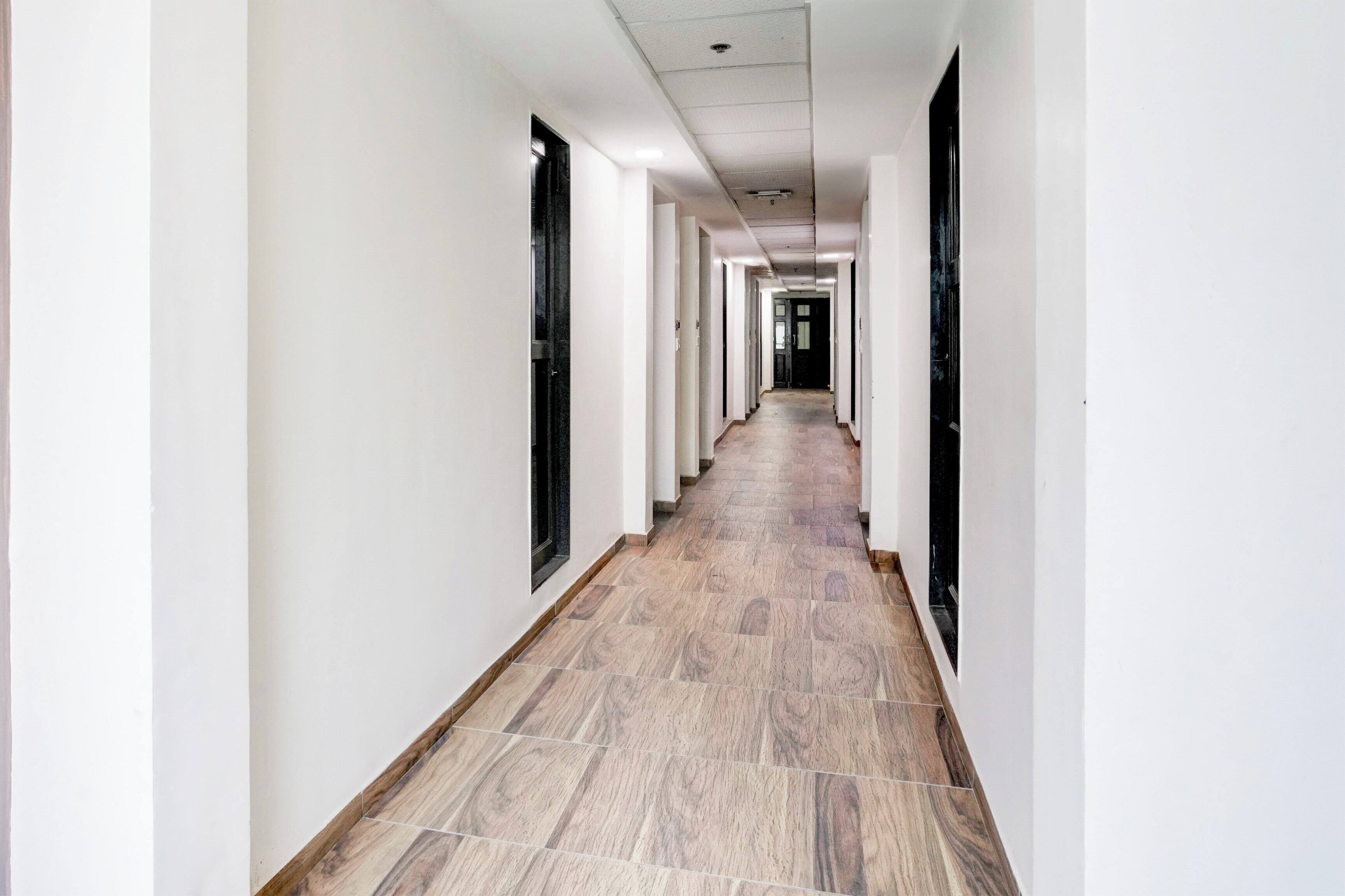 A long, narrow hallway with white walls and a tiled floor, leading to a dark door at the end.