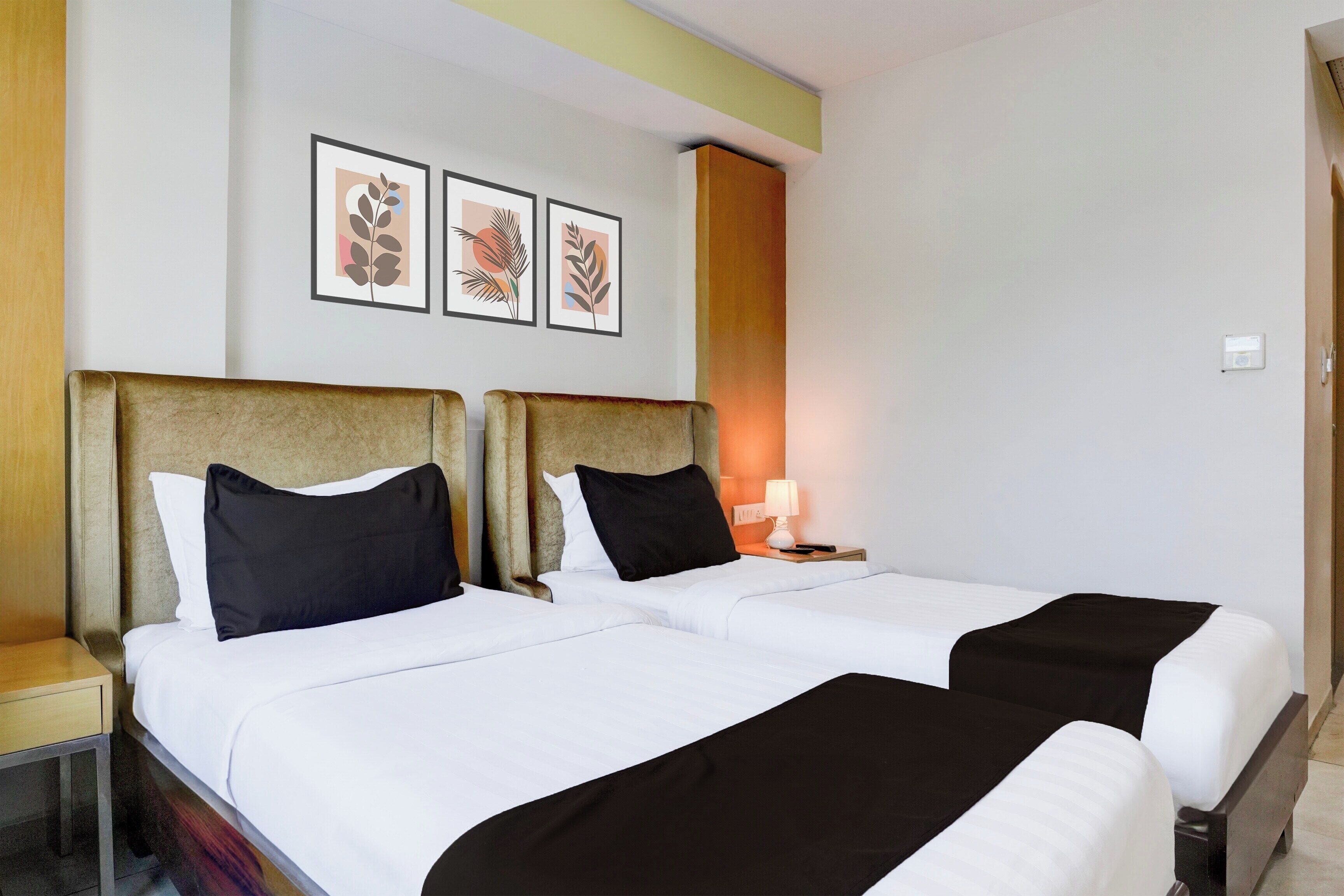 A hotel room with two beds, a nightstand with a lamp, and three framed artworks on the wall.