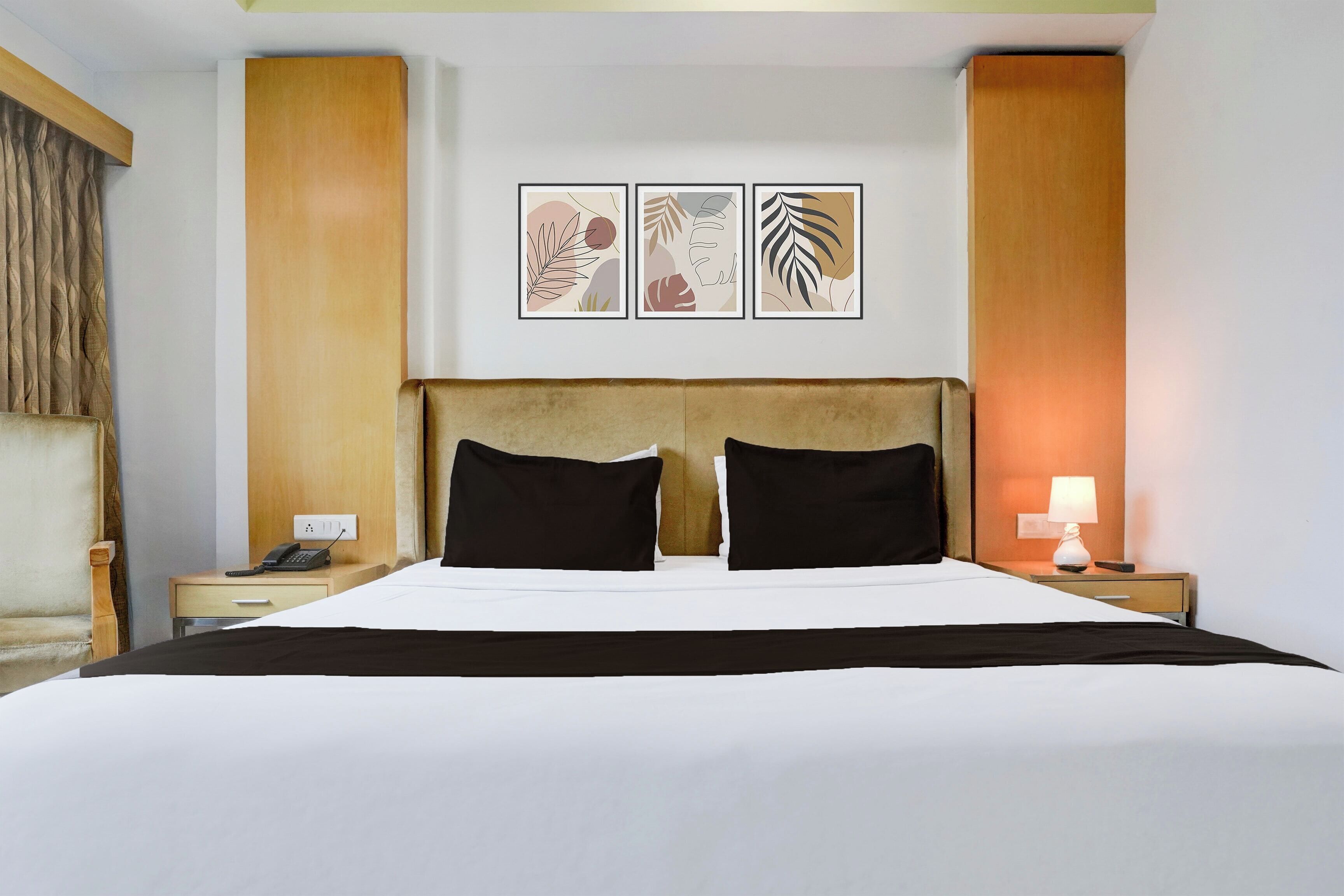 Habitación de hotel con una cama grande, dos mesitas de noche, una lámpara y tres cuadros en la pared.