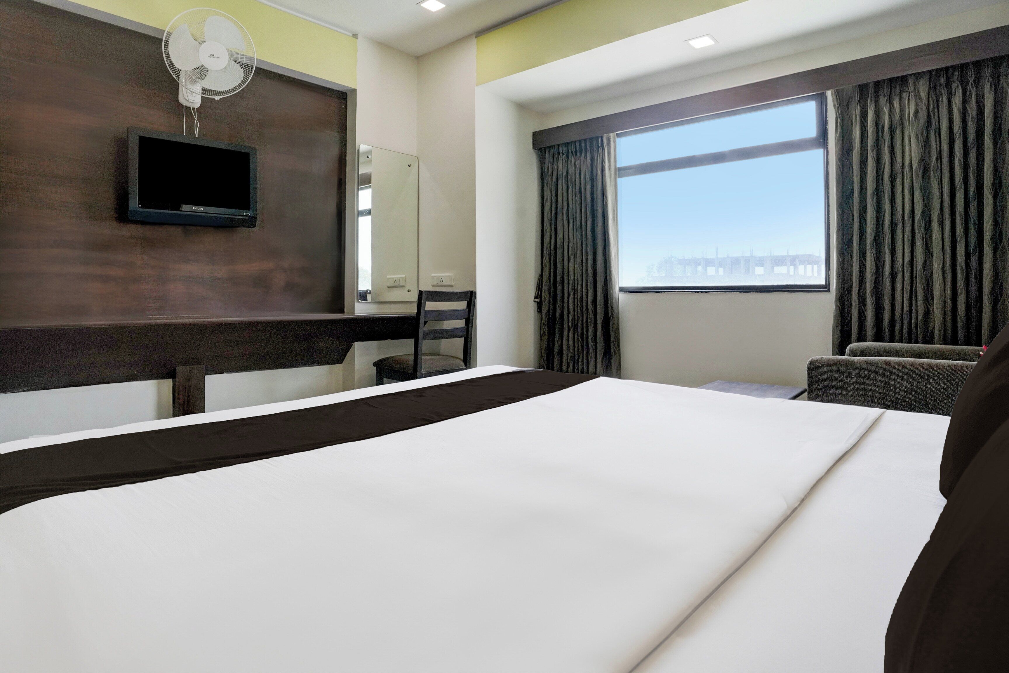 A hotel room with a bed, a desk, a chair, a television, and a window with curtains.