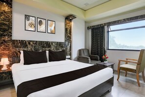 A modern hotel room with a large bed, a seating area with a sofa and chairs, a desk, and a large window offering a view. - Townhouse Anand Formerly Hotel (Anand)