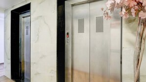 Un ascenseur doté d’un écran numérique et d’un panneau de commande, situé dans un couloir dont le mur est recouvert de marbre et le sol, de bois.