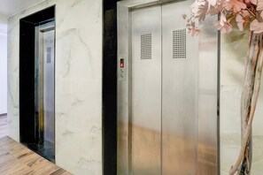 An elevator with a digital display and a control panel, located in a hallway with a marble wall and a wooden floor.