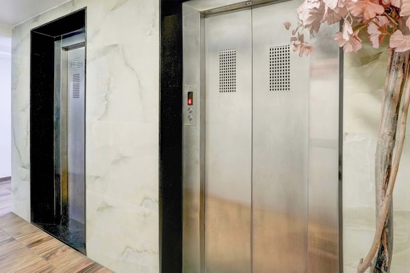 An elevator with a digital display and a control panel, located in a hallway with a marble wall and a wooden floor.