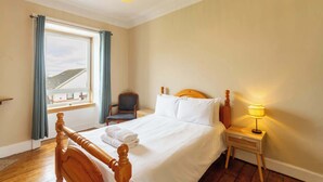 A hotel room with a bed, a chair, a nightstand, a window with curtains, and a view of the outside. - Serene 2BDR Flat Near Edinburgh Old Town (Edinburgh)