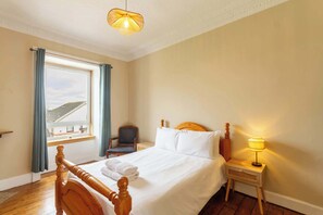 Ein Hotelzimmer mit Bett, Sessel, Nachttisch, Fenster mit Vorhängen und Blick ins Freie.