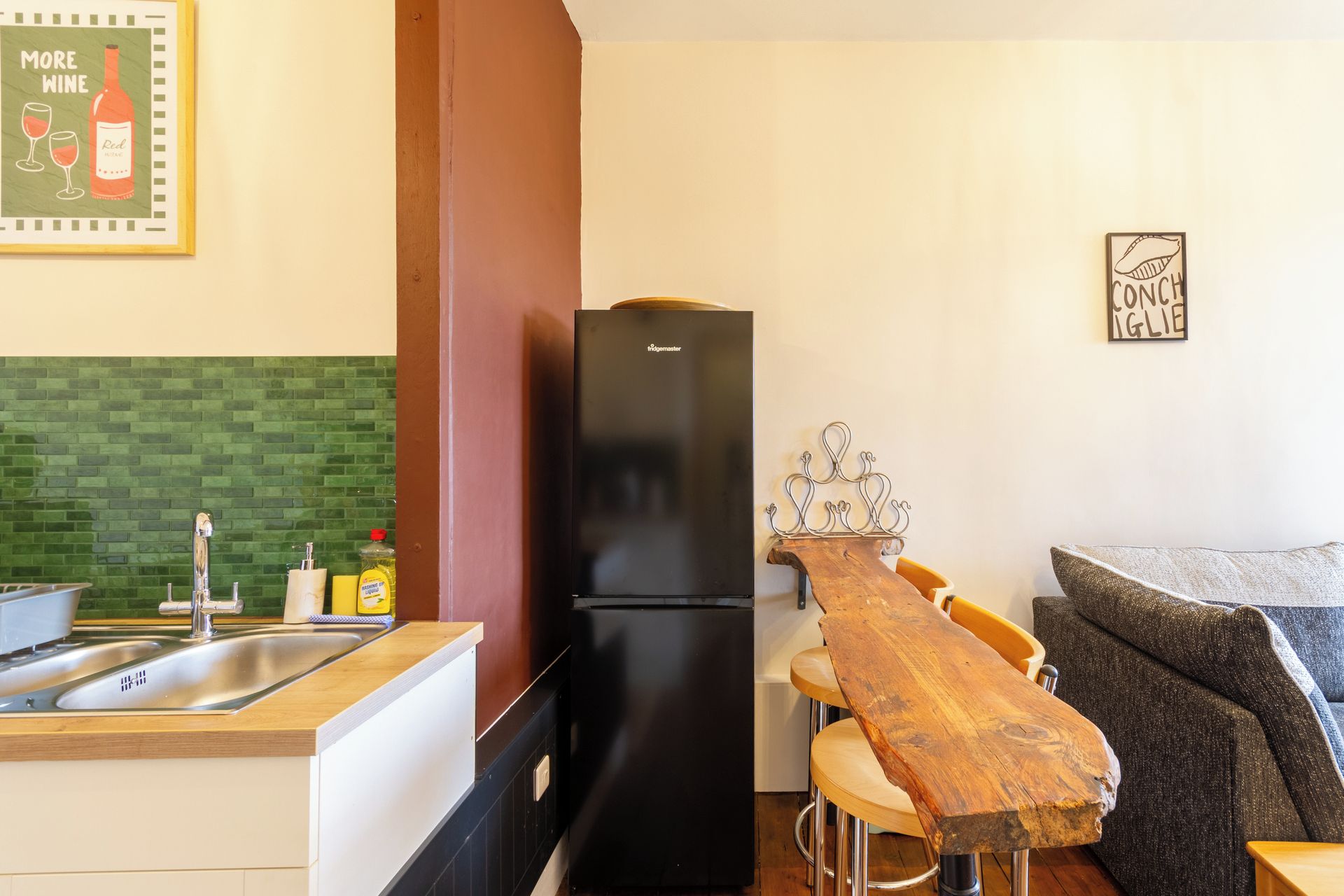 Een kleine keuken met een zwarte koelkast, een houten bar en een groene tegelachtergrond.