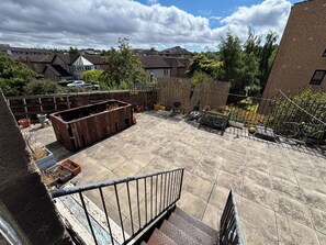 Eine Dachterrasse mit Metallgeländer, Blumentöpfen und Blick auf umliegende Gebäude.