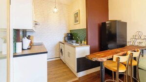 A compact kitchen with a wooden bar counter, a black refrigerator, a washing machine, and a hanging light fixture. - Serene 2BDR Flat Near Edinburgh Old Town (Edinburgh)