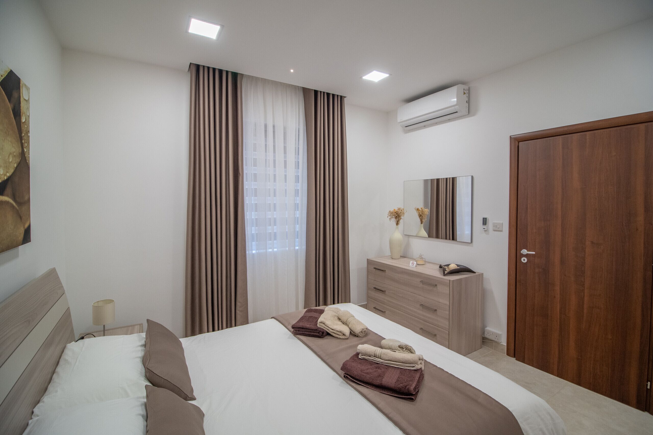 Une chambre à coucher moderne, équipée d’un lit, d’une commode, d’un miroir et d’un appareil de climatisation.