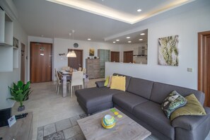 Ein modernes Wohnzimmer mit grauem Sofa, einem Essbereich mit Tisch und Stühlen und einer Küche im Hintergrund.