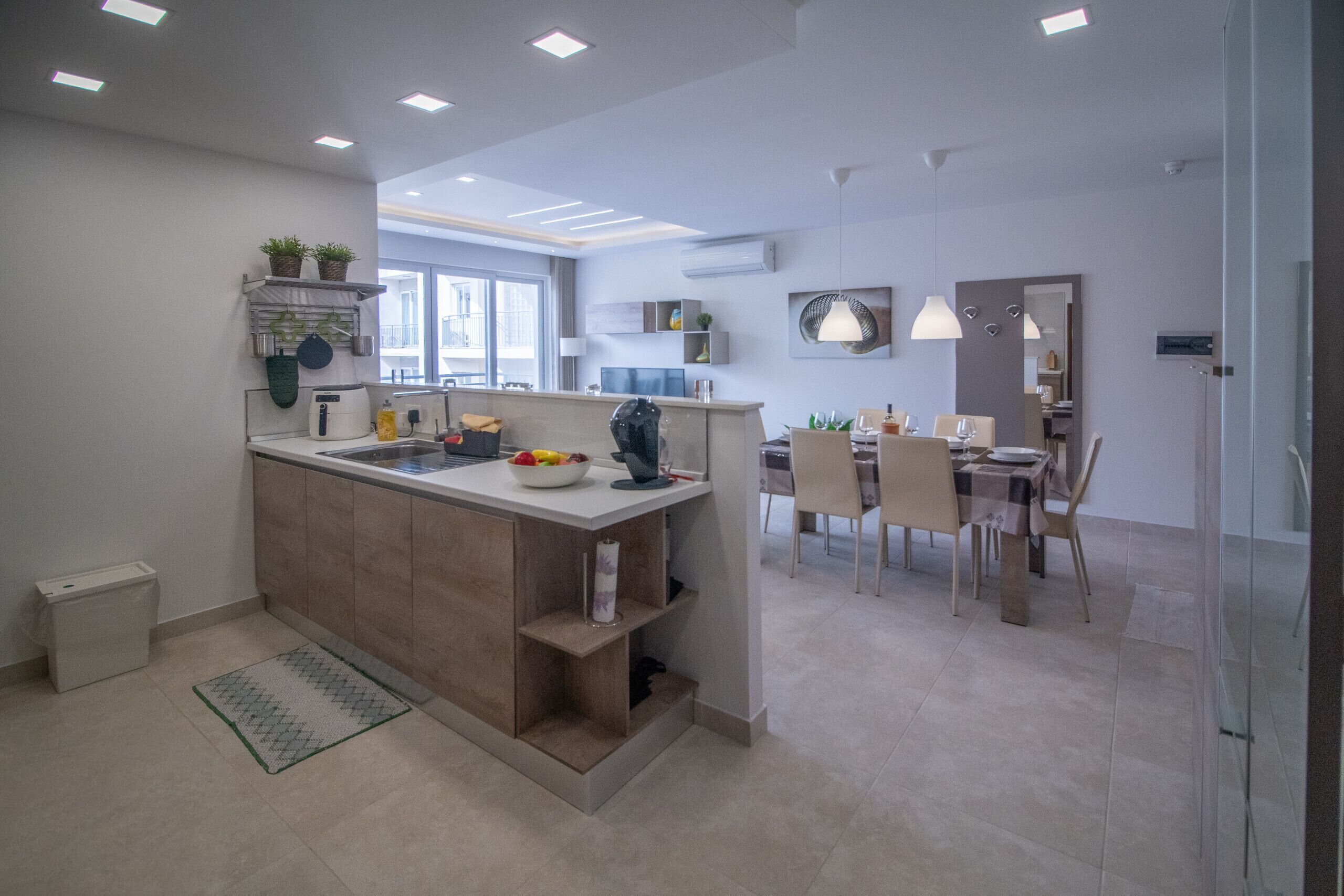 A modern kitchen with a central island, dining area with chairs, and a large window.