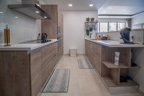 Eine moderne Küche mit Holzausstattung, einer Edelstahl-Dunstabzugshaube und einem eingebauten Backofen. Es gibt zwei Spülen, eine Kaffeemaschine und einen Mülleimer.