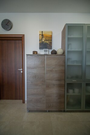 A wooden door with a clock, a cabinet with a wine bottle and glasses, and a glass-fronted cabinet with plates. - Bright 3 bedroom with terrace and pool GZ-MAVE1-1 (Marsalforn)