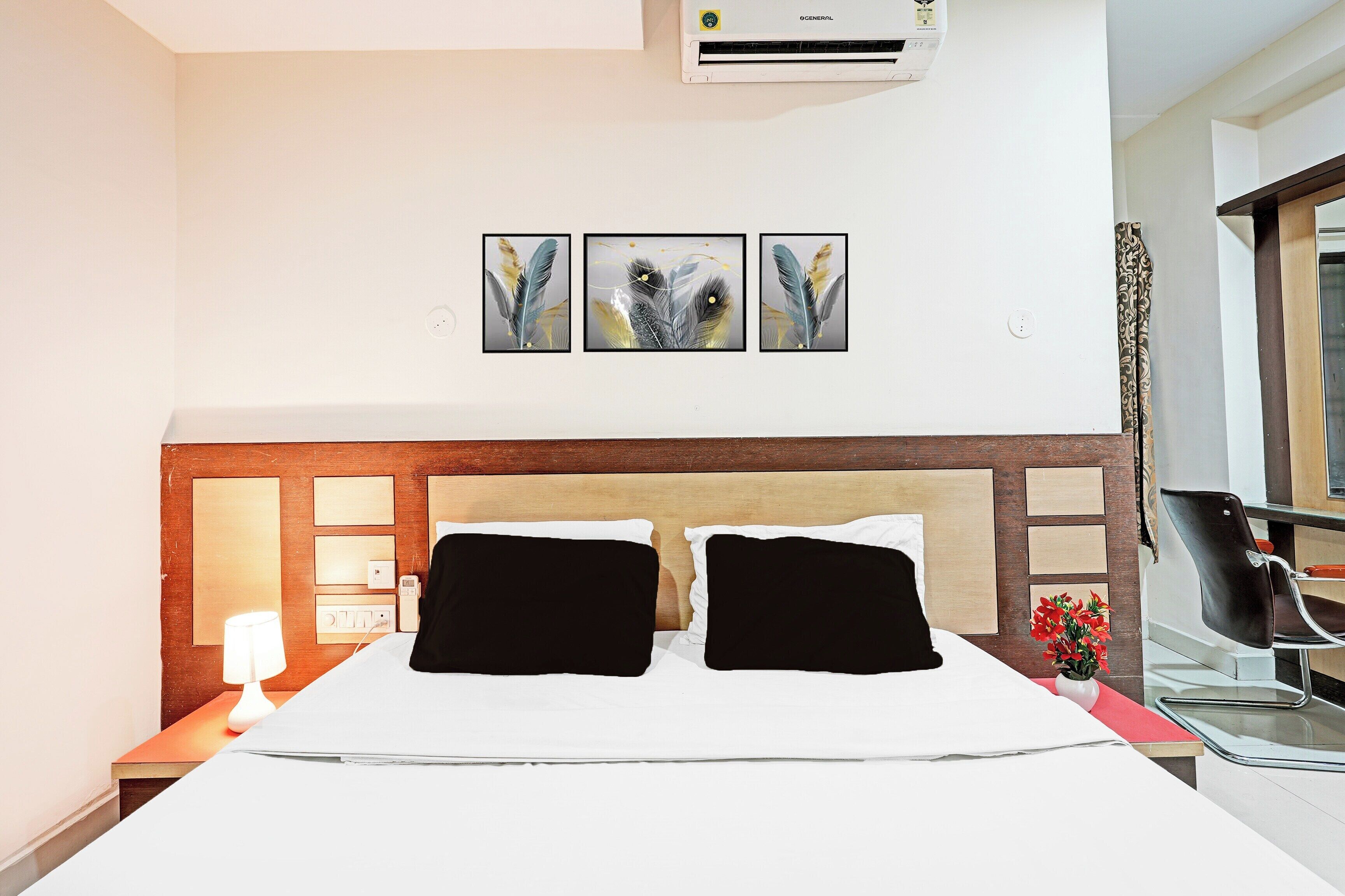 Habitación de hotel con cama, mesita de noche, lámpara, silla y aire acondicionado de pared.