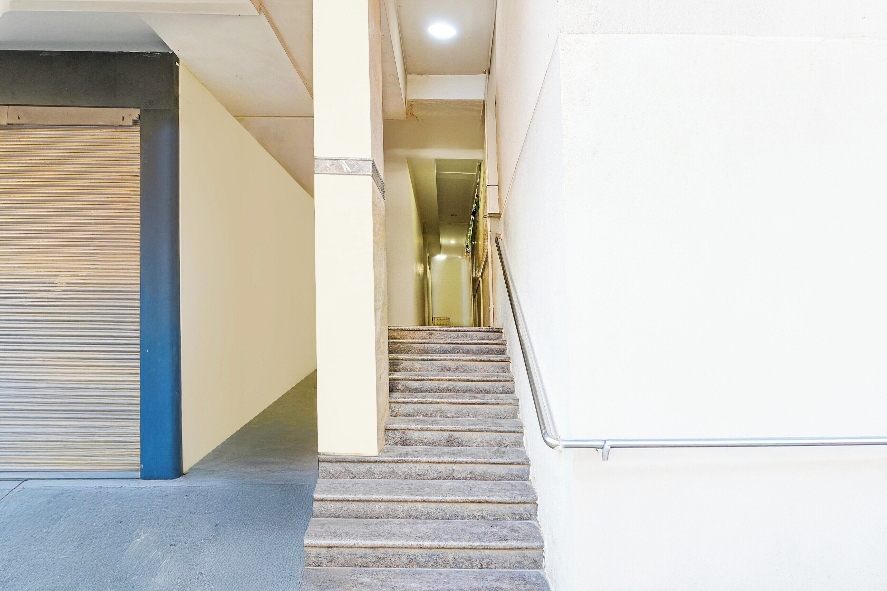A staircase leading to an interior space with a closed shutter door on the left and a metal railing on the right.