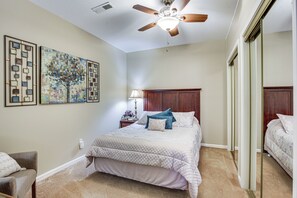 A bedroom with a bed, a ceiling fan, a nightstand with a lamp, and two framed artworks on the wall.