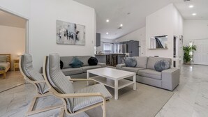 Ein modernes Wohnzimmer mit einer Couch, zwei Sesseln, einem Couchtisch und einer Küche im Hintergrund.