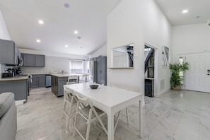 A modern kitchen with grey cabinets, a white dining table, and a large island. - Poolside Fun 8 Mi to Disney! Family Getaway (Kissimmee)