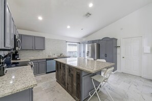 A modern kitchen with grey cabinets, a granite countertop, and a built-in island with seating. - Poolside Fun 8 Mi to Disney! Family Getaway (Kissimmee)