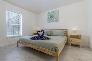 A bedroom with a wooden bed, a nightstand, a wall-mounted lamp, and a window with blinds. - Poolside Fun 8 Mi to Disney! Family Getaway (Kissimmee)