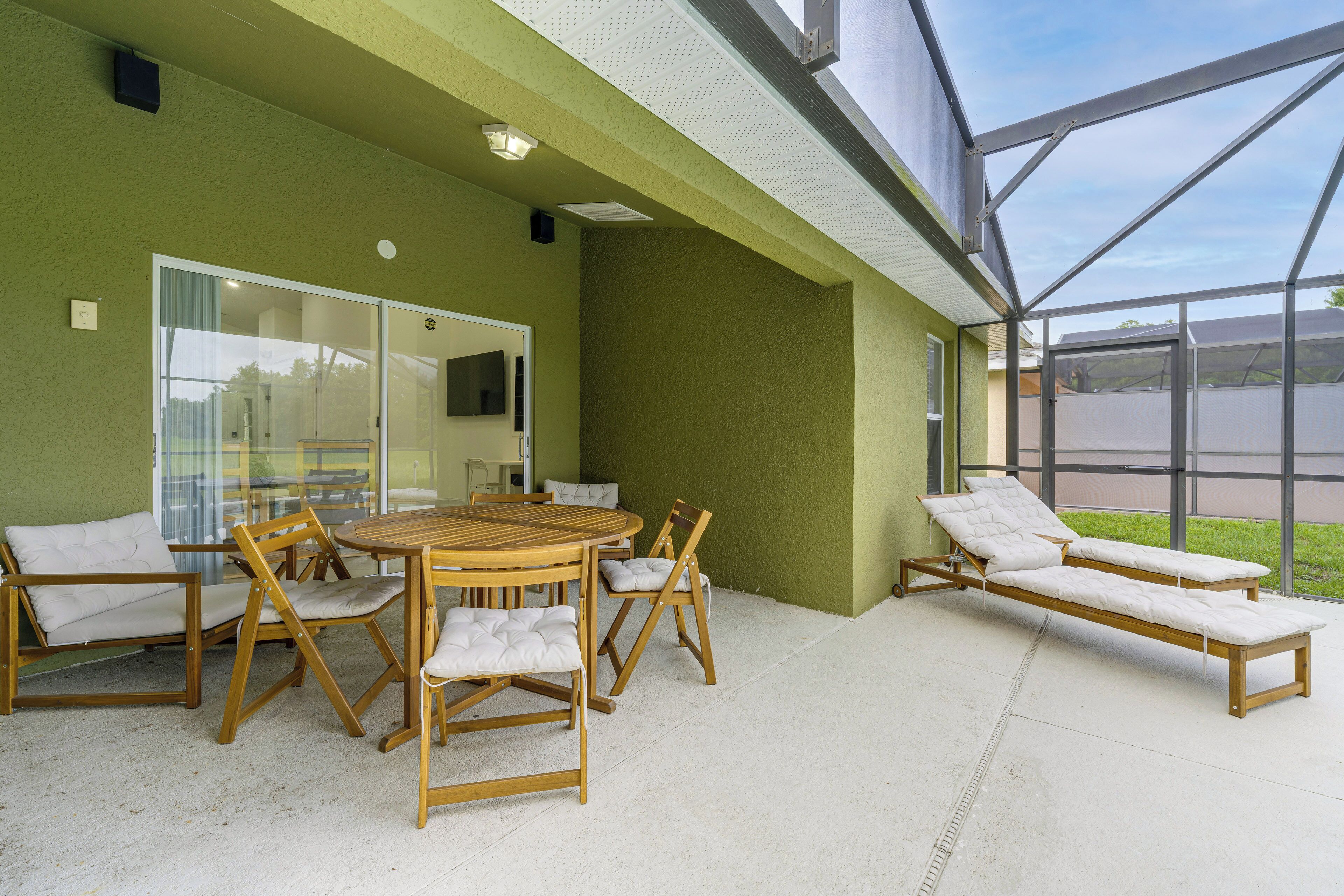 Een terras buiten met een houten tafel en stoelen, een glazen deur naar binnen en een glazen constructie met uitzicht op de omgeving.