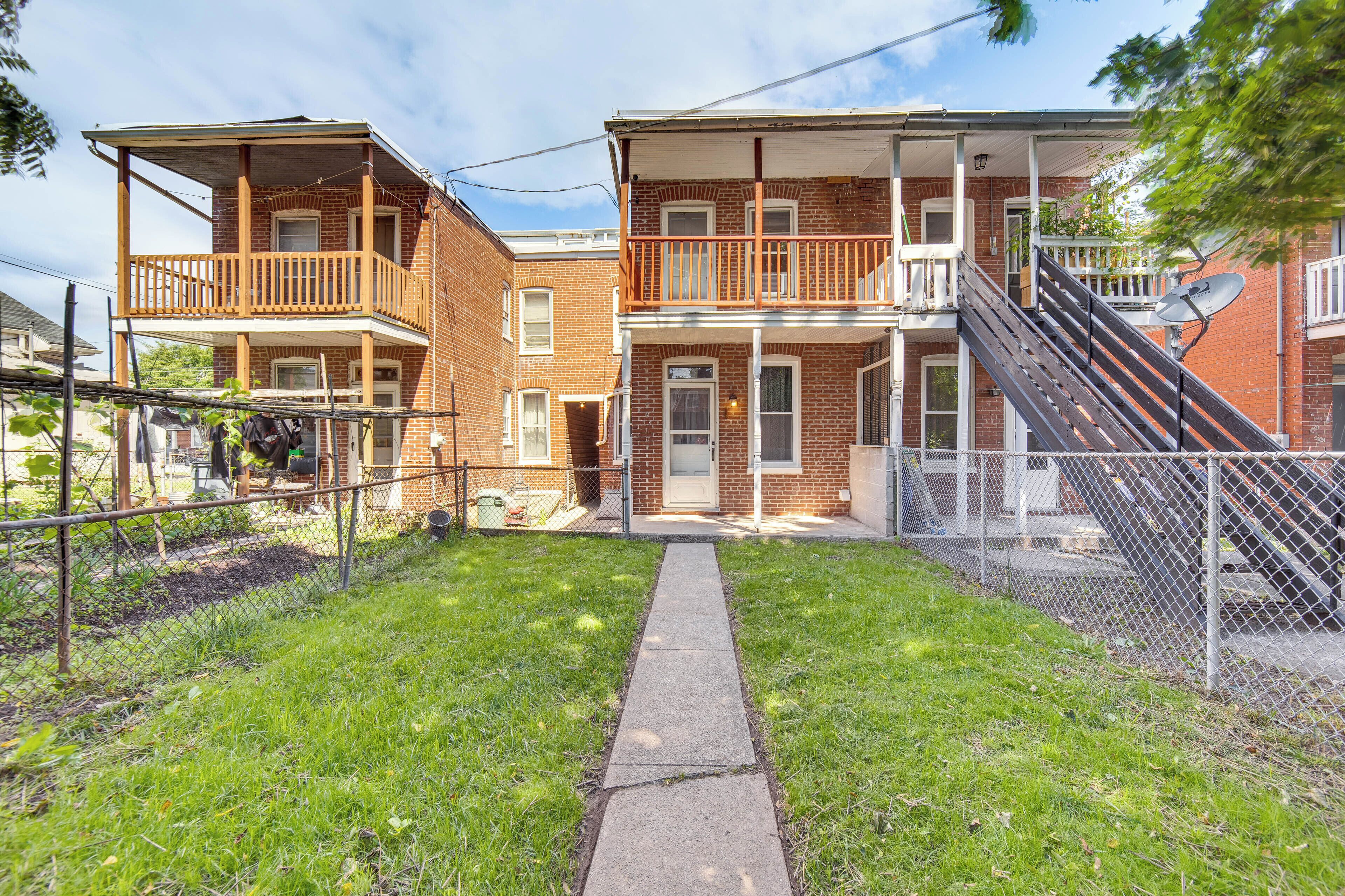 A two-story brick building with a front porch, a staircase, and a fenced yard.