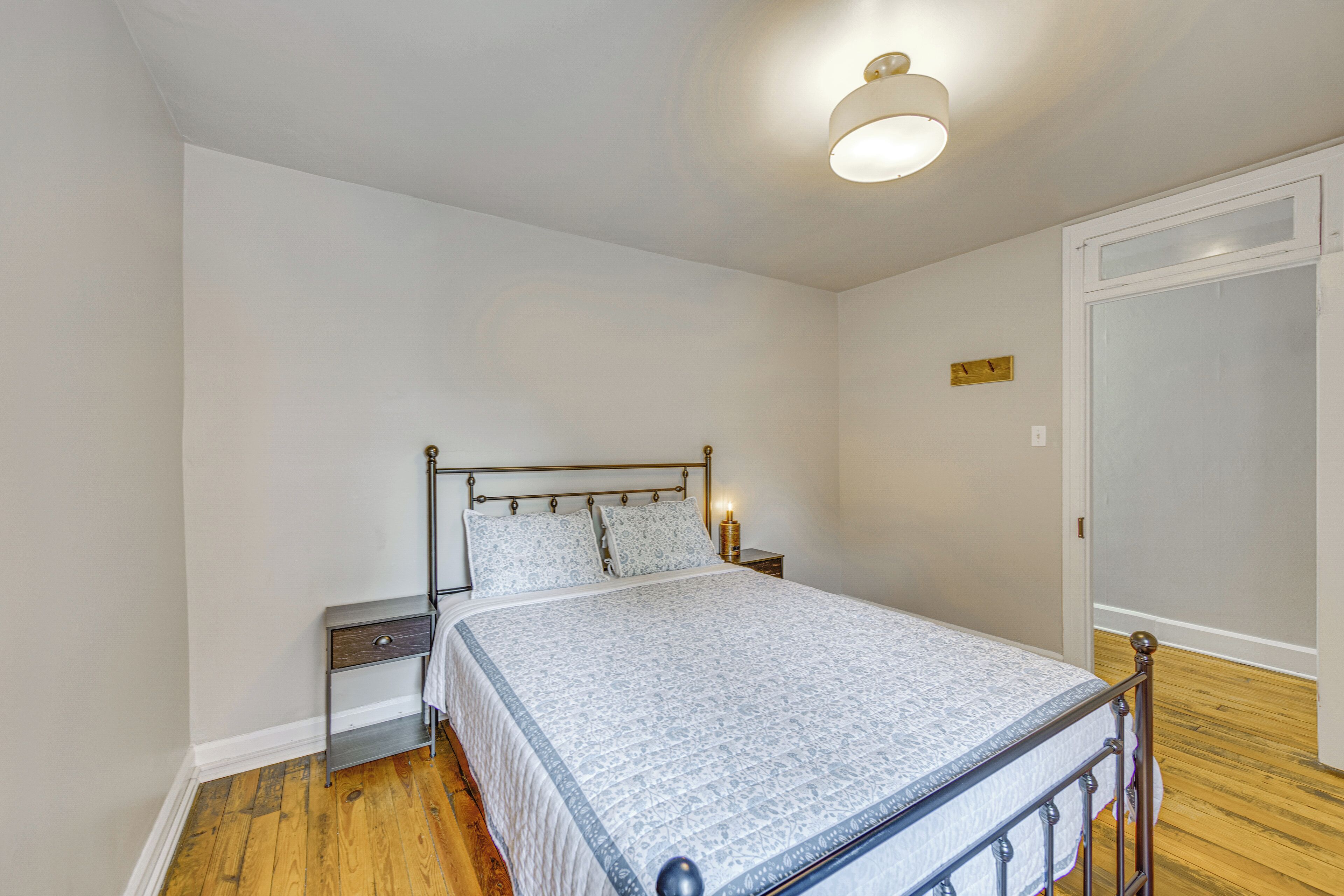Un dormitorio con una cama, mesitas de noche, una lámpara de noche, un reloj de pared y una puerta.