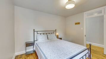 Un dormitorio con una cama, mesitas de noche, una lámpara de noche, un reloj de pared y una puerta.