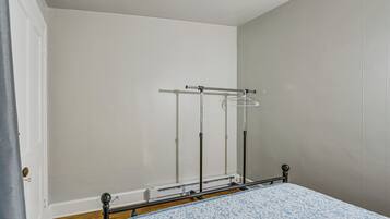 Ein Schlafzimmer mit einem Bett, einem Metallschrank und einem an der Wand befestigten Wäscheständer.