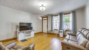 A living room with a flat-screen TV, leather sofa, and a wooden floor.