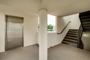 Un coin d’un bâtiment avec un sol en béton, une porte d’ascenseur métallique et un escalier muni d’une main courante.