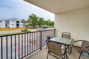 Un balcon avec une table et des chaises, donnant sur un parking et une rangée d’immeubles.