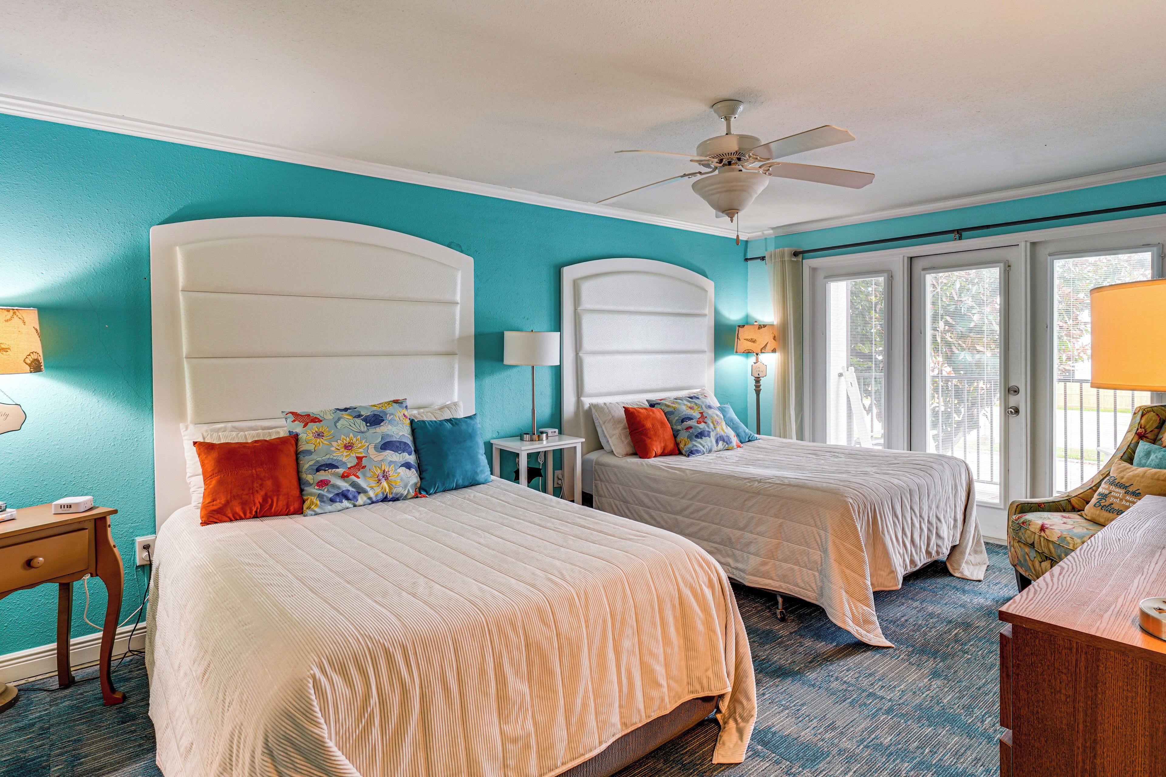 A hotel room with two beds, a ceiling fan, and a view of the outdoors through the windows.