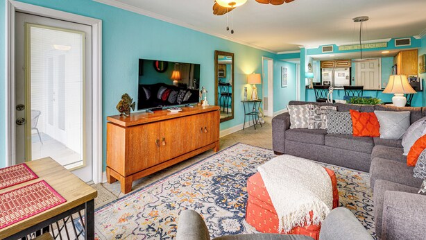 A living room with a wooden cabinet, a grey sofa, a patterned rug, and a ceiling fan. - Walk to Beach! Biloxi Condo w/ Community Perks (Biloxi)