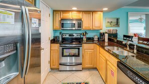A kitchen with stainless steel appliances, wooden cabinets, a granite countertop, and a tiled floor. - Walk to Beach! Biloxi Condo w/ Community Perks (Biloxi)