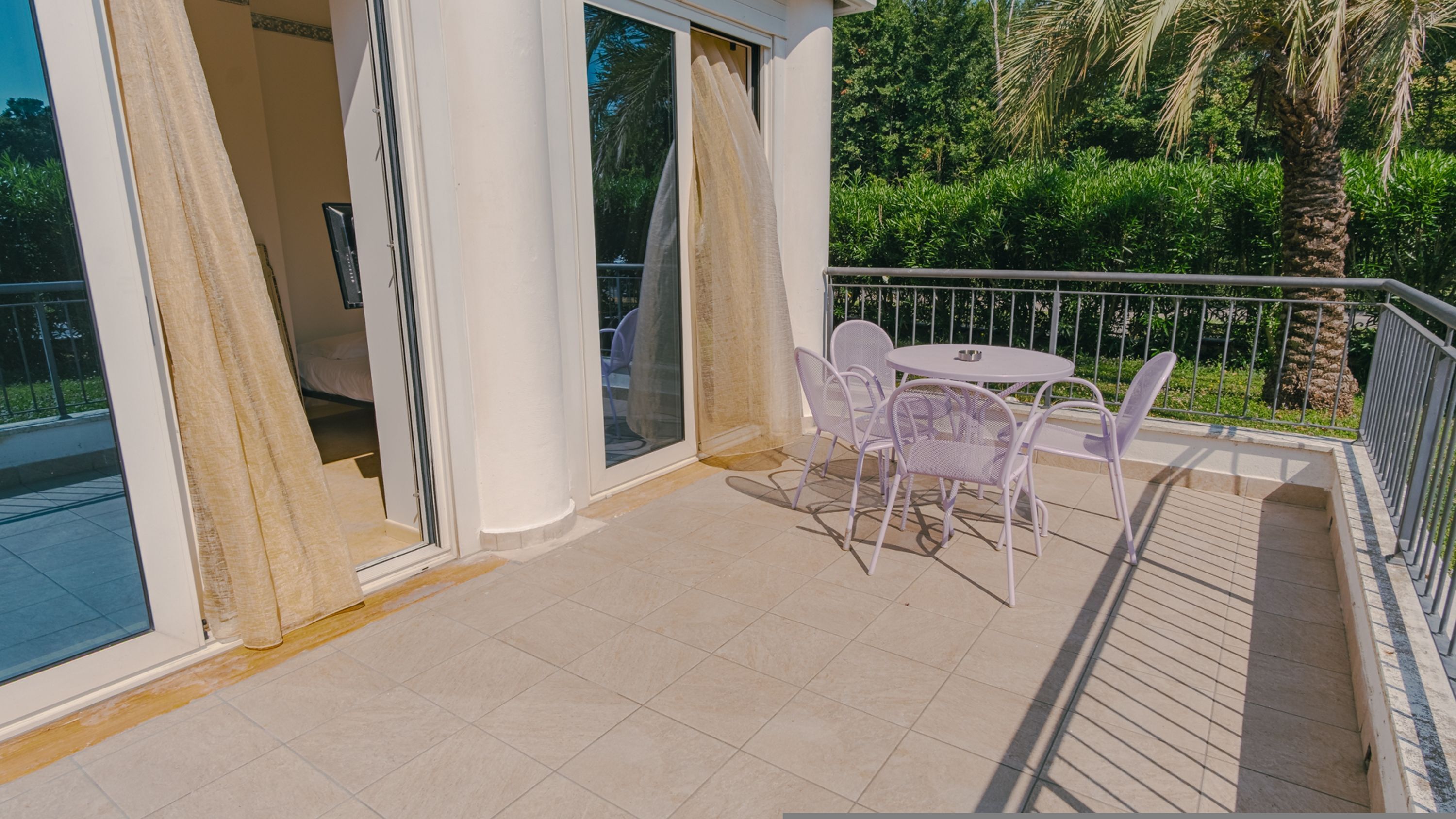 A balcony with a table and chairs, a sliding glass door, and a view of greenery.