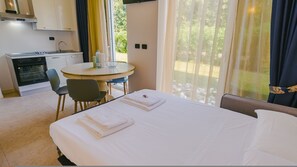 A hotel room with a bed, a dining table, chairs, a kitchen area, and a view through the window. - 11 Relais du Lac Charme - Italian Homing (Desenzano del Garda)