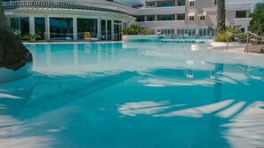Ein klares, blaues Schwimmbecken mit Rettungsboje, umgeben von einem Gebäude mit mehreren Balkonen und Palmen.