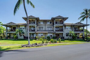 A multi-story hotel with balconies, a covered front porch, and a well-maintained garden. - Halii Kai Condo Close in Proximity to Ocean/Pool (Waikoloa Village)